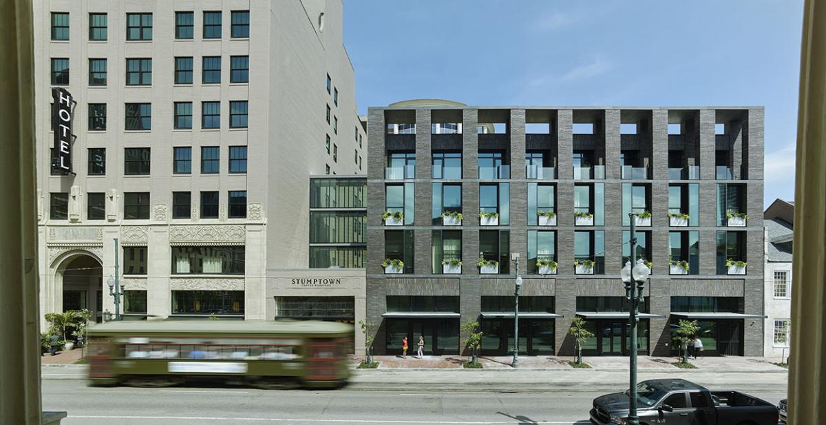 Exterior shot of a few commercial buildings on a street with a bus driving past the buildings and a grey truck parked on the other side of the street.