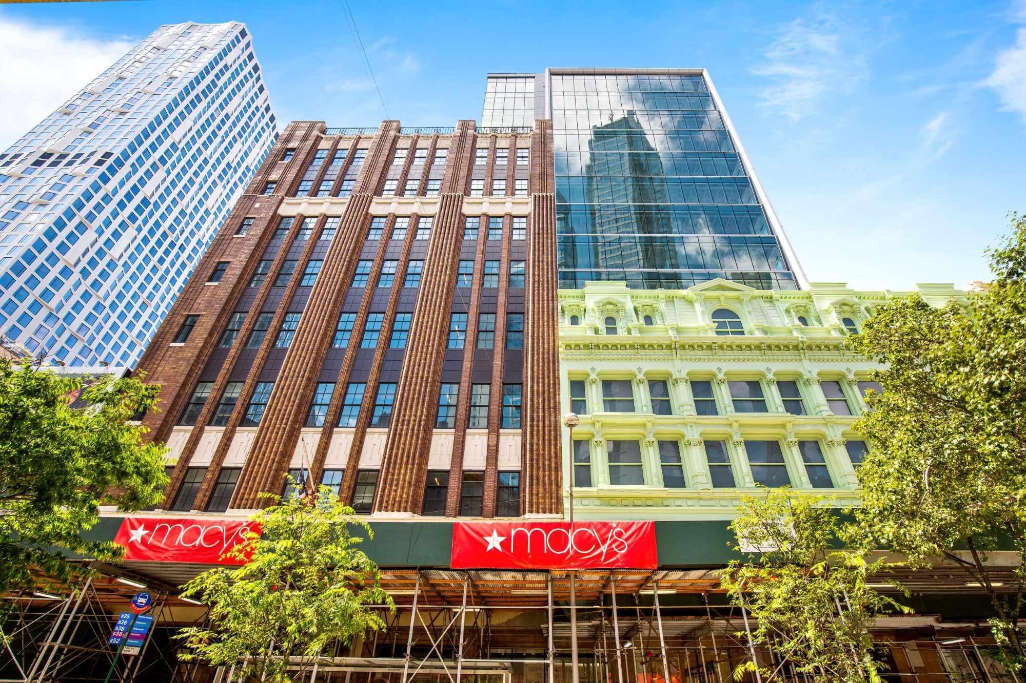 This Macy’s storefront has a red banner with its logo on it, and there are skyscrapers behind construction rafters.