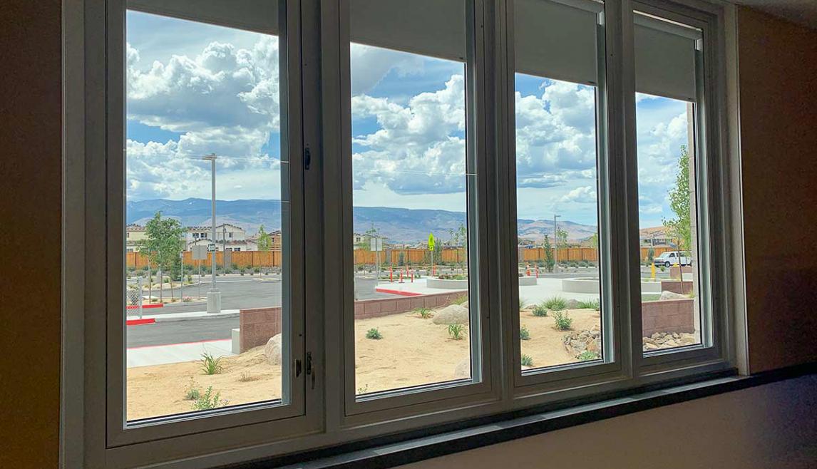 Four windows overlook a parking lot. There are mountains in the distance, and clouds cover the blue sky.