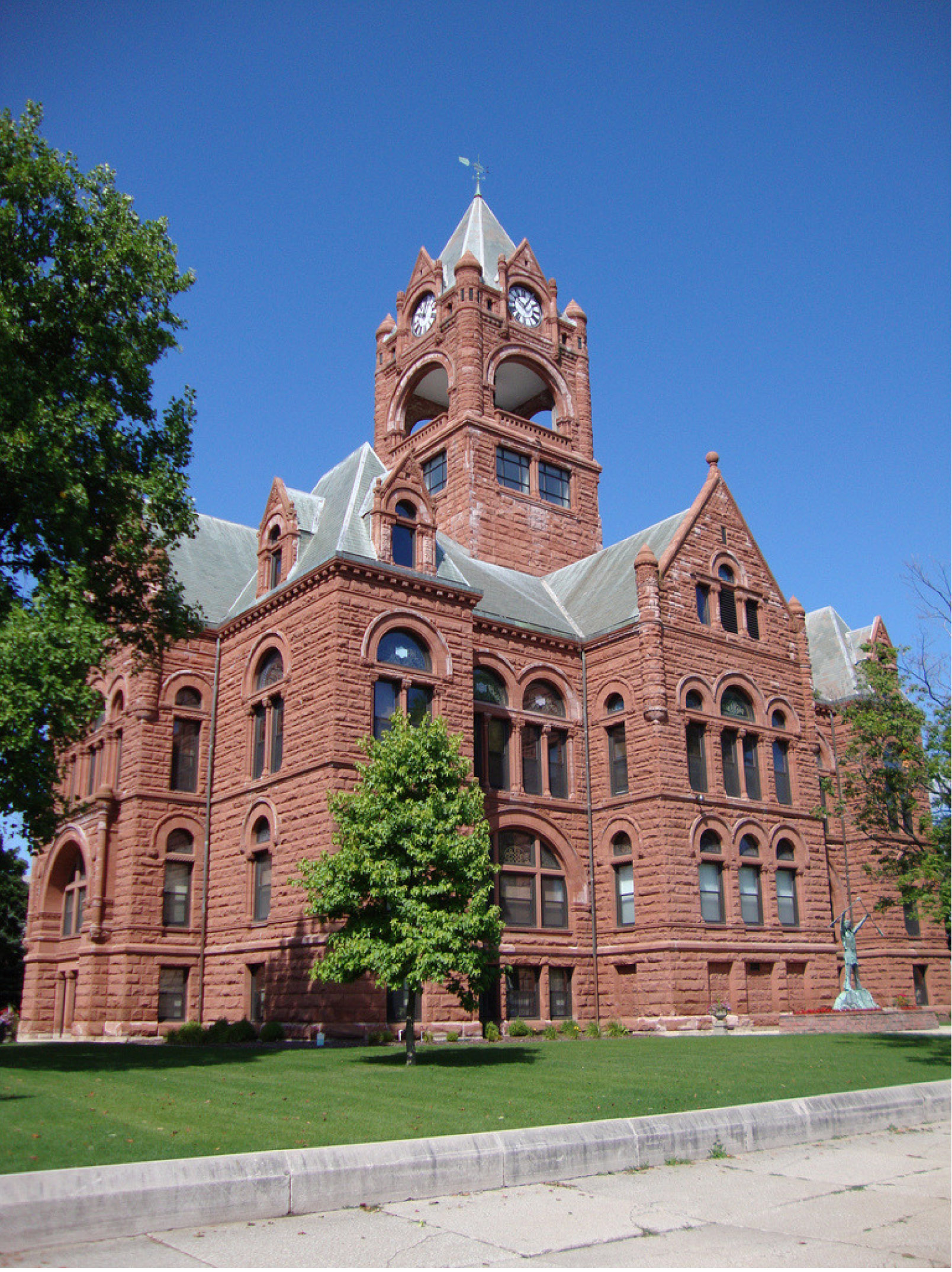 This brick courthouse building has green grass and green trees surrounding the building. 