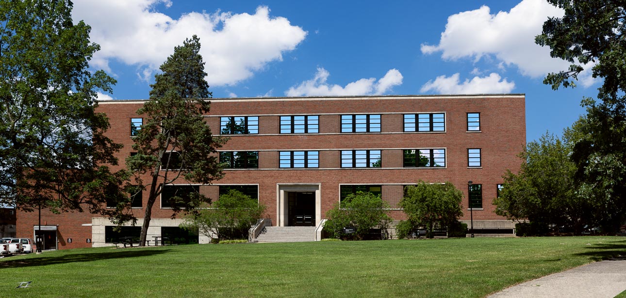 Front view of brick building with trees and grass in front
