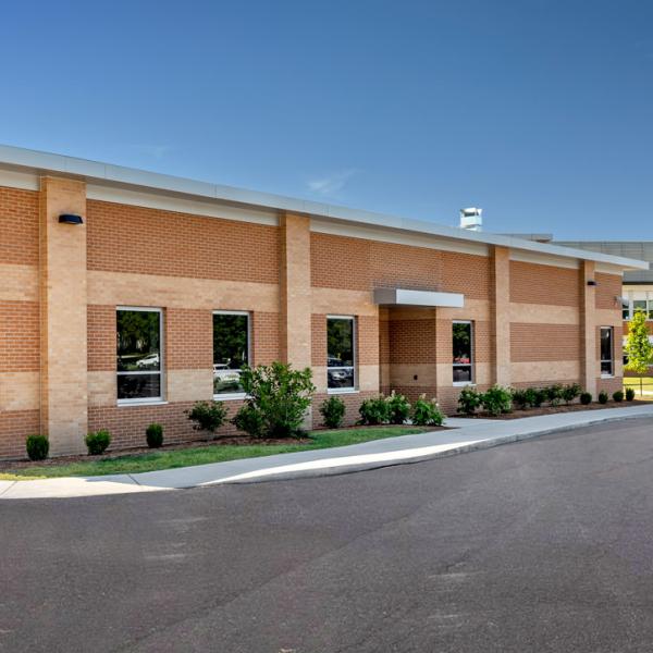 Exterior brick building featuring FEMA windows with a parking lot in front and blue sky in the background.