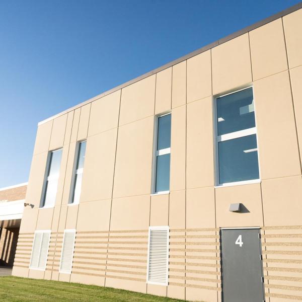 Modern school building with beige and brick facade under a clear blue sky. Manicured lawn create a peaceful, sunny atmosphere.