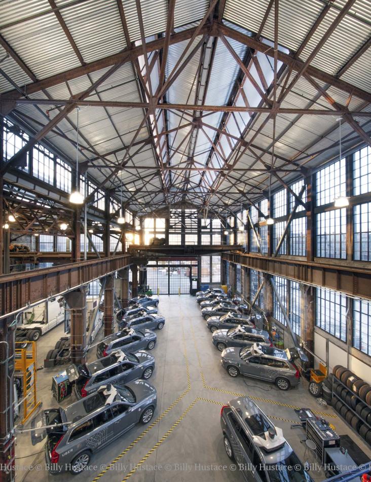 This large building holds vehicles inside. With a lot of exposed steel frames, the building also features large glass windows and hanging light fixtures. 