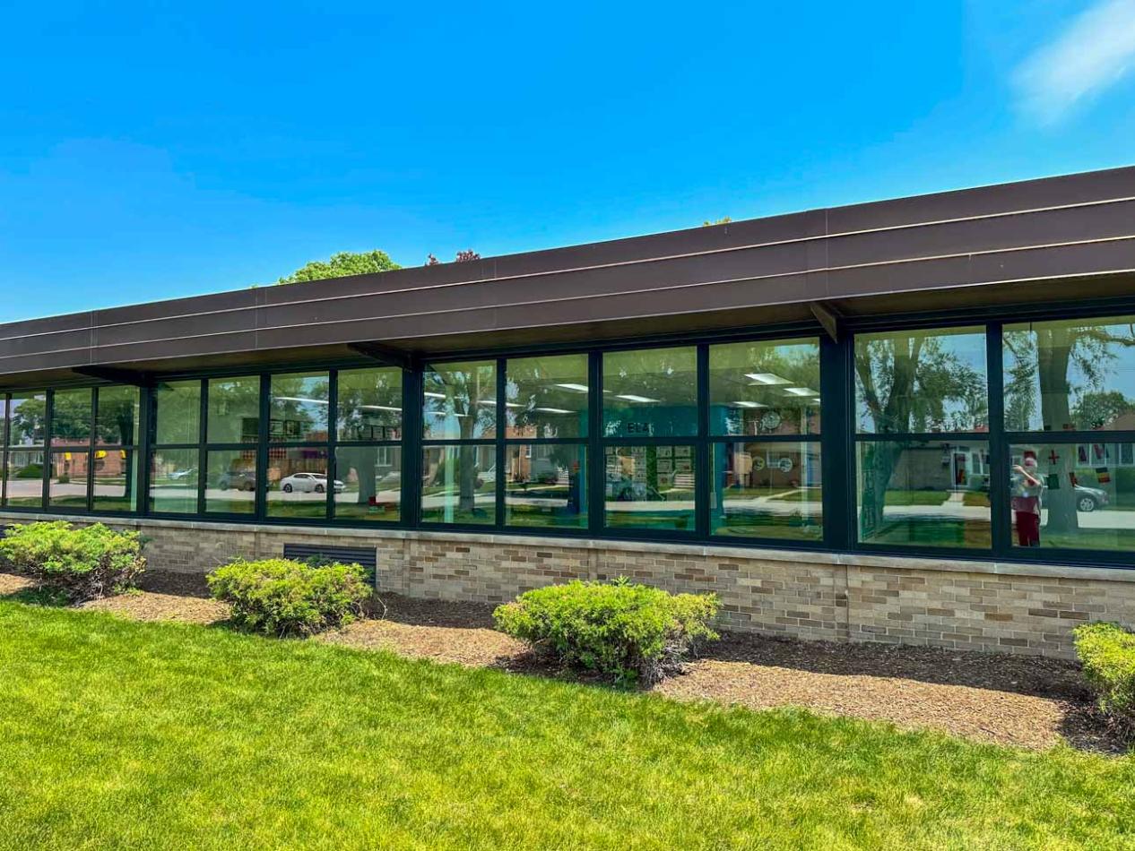 Building facade showcasing large dark bronze anodized windows, complemented by a grassy landscape in front.