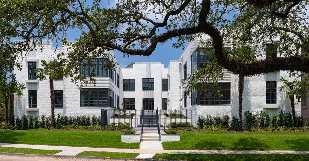 Exterior of white brick building with large steel replica windows and trees in background