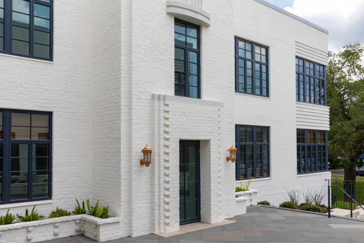 A white building with windows and a courtyard, showcasing WINCO’s NC82 Terrace Doors that meet hurricane safety standards.