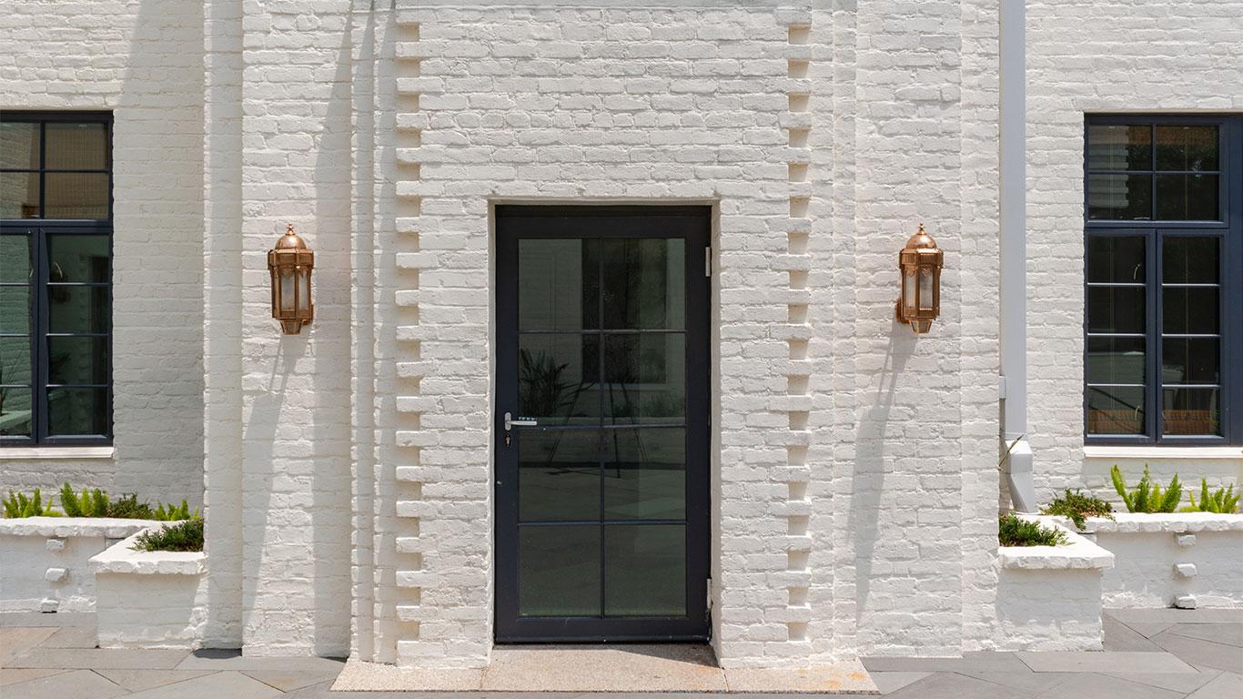 A white brick building featuring a large door, equipped with WINCO’s NC82 Terrace Doors for hurricane resistance.