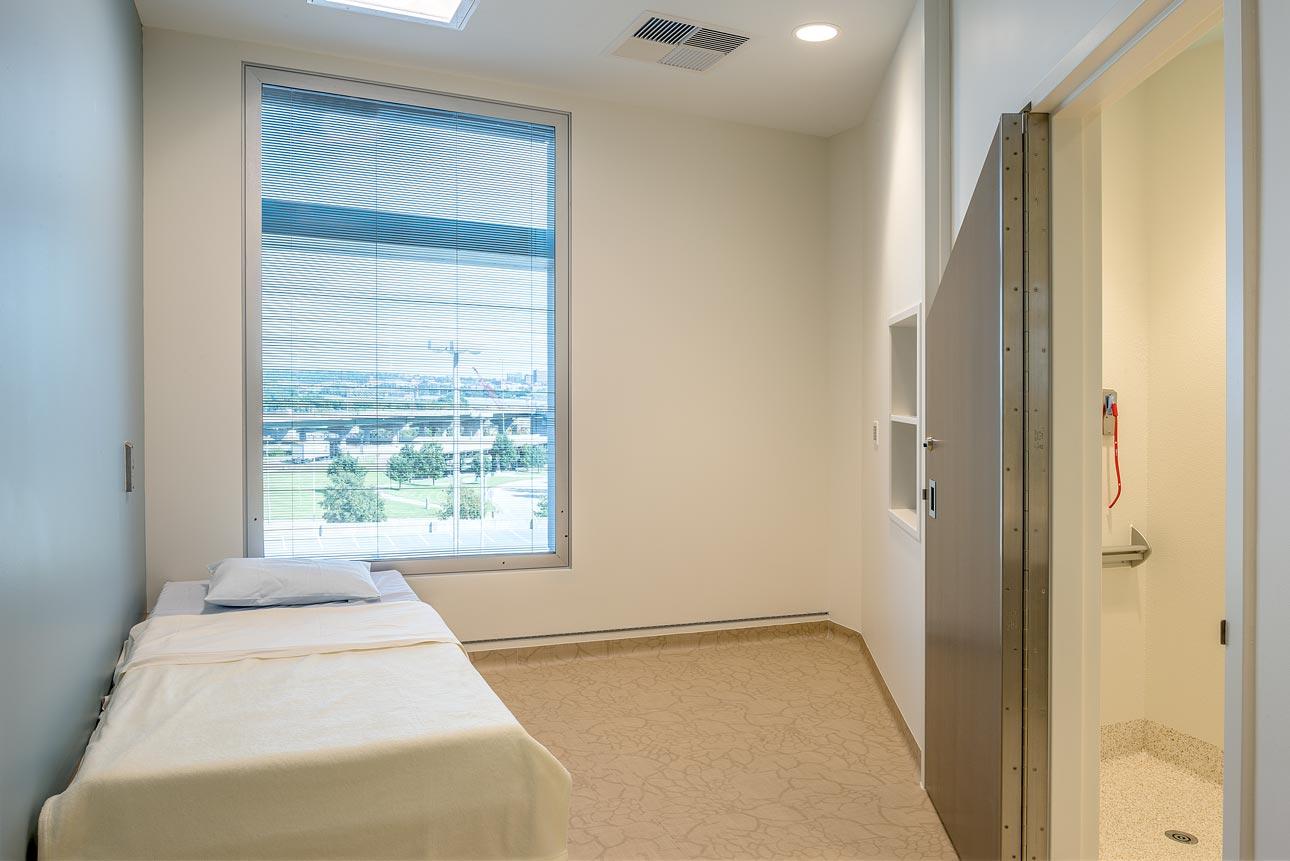 A behavioral care patient room with a bed and a window, equipped with human impact resistant windows for safety. 
