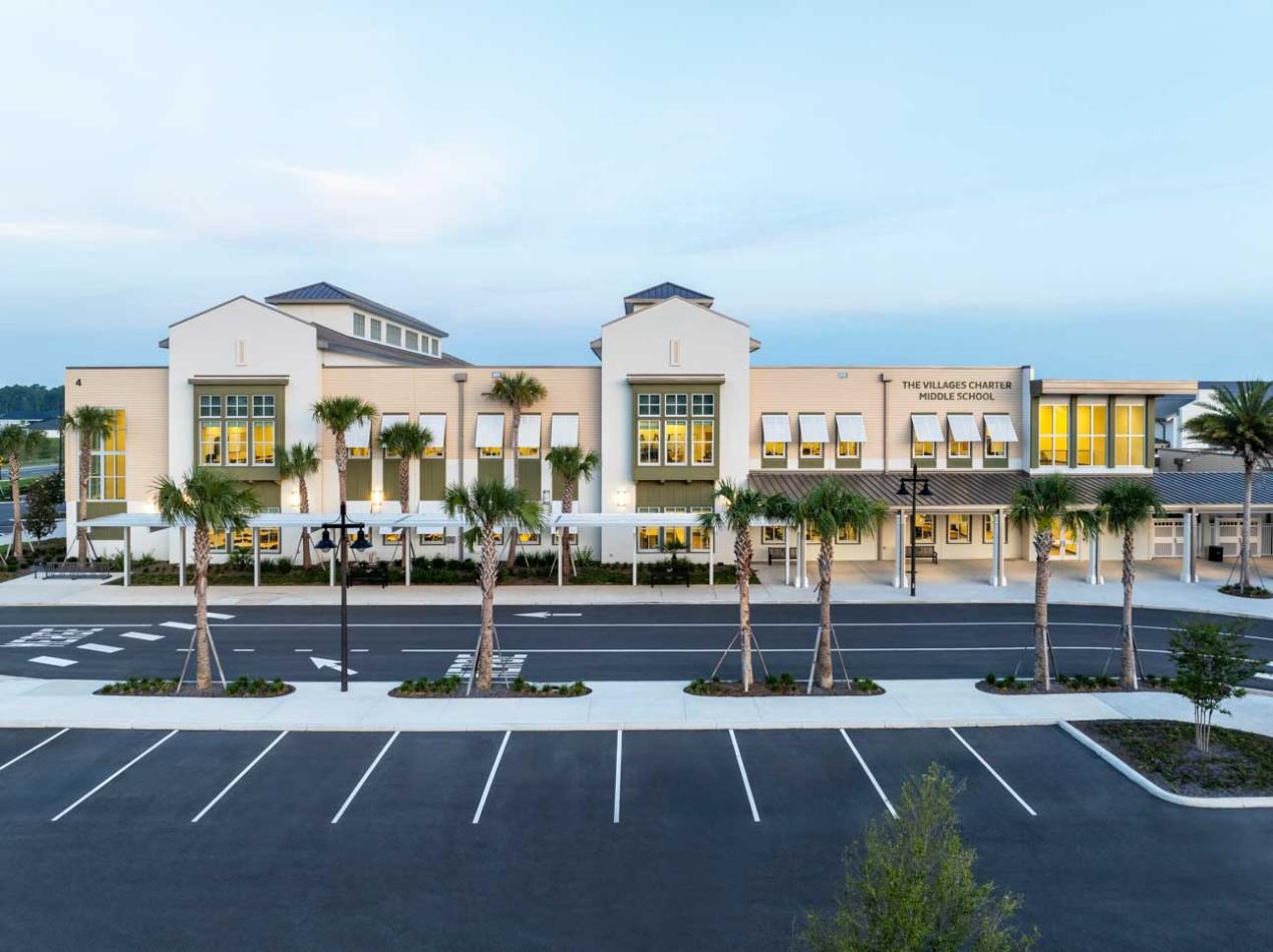 Front of school building at dusk with palm trees in front.