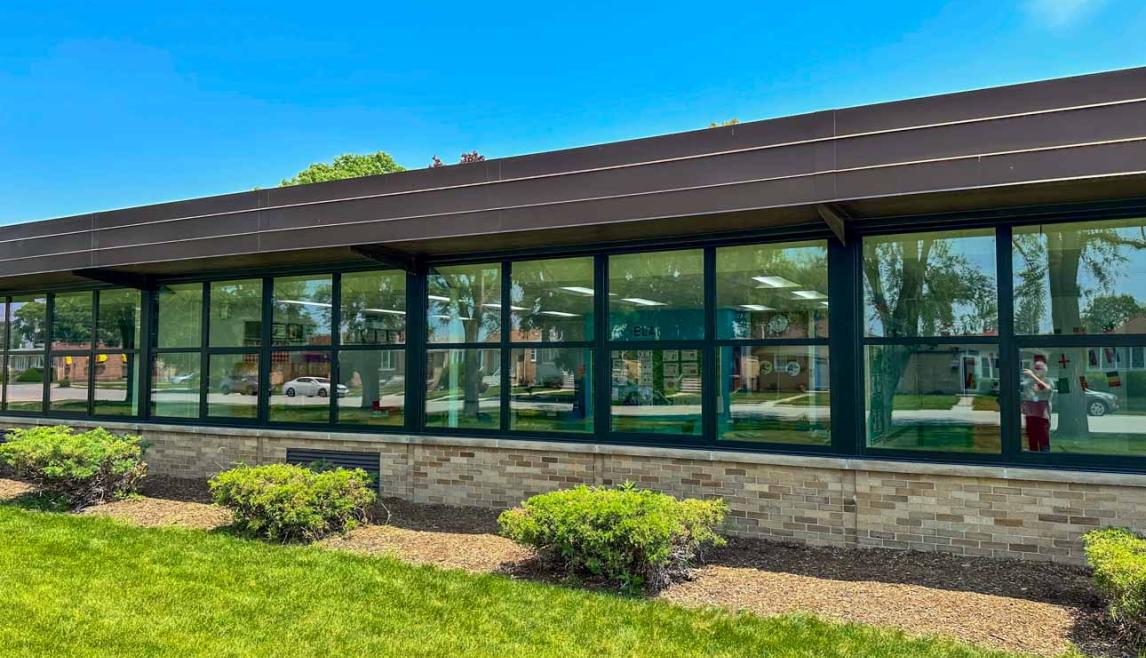 Building facade showcasing large dark bronze anodized windows, complemented by a grassy landscape in front.