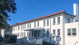 Exterior white brick building featuring historic replica windows with field in front and blue sky in the background.